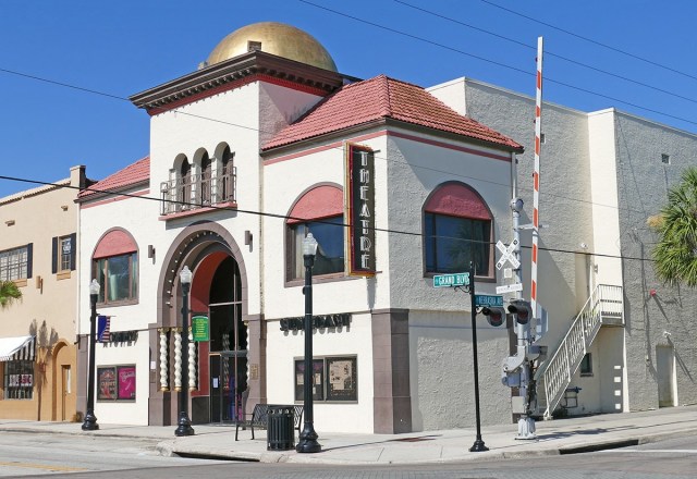 Corner street-view of a small theater with a gold dome, red-tiled roof, and arched windows along Grand Blvd.